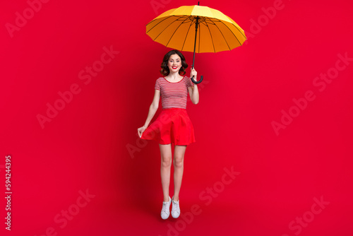 Full length portrait of excited crazy lovely person arm hold umbrella jumping flying isolated on red color background