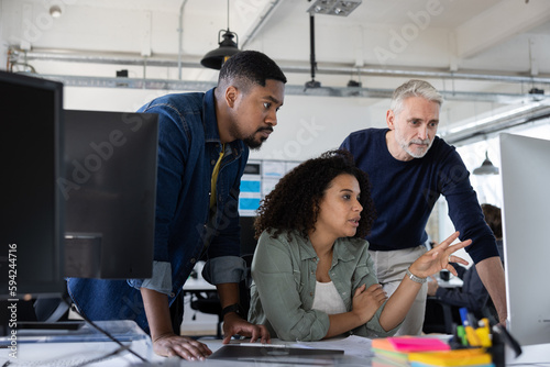 Group of coworkers meeting round a desktop computer in discussion