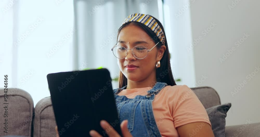 Asian woman, tablet and relax on sofa in living room for social media or streaming entertainment at home. Happy female relaxing on lounge couch browsing, scrolling or searching on technology indoors