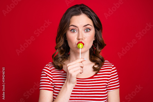 Portrait of gorgeous adorable cute sweet lady wear trendy clothes hand hold taste delicious candy isolated on red color background