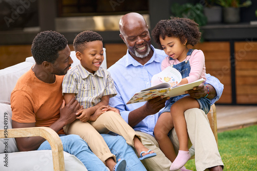 Smiling Multi-Generation Family Reading Book In Garden Together