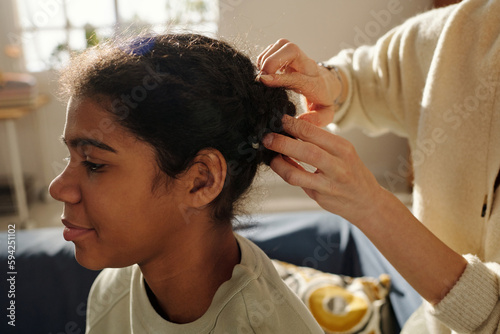 Close-up of mother making hairstyle to her African American adopted daughter preparing her for school