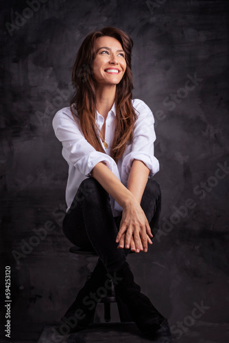 Smiling brunette businesswoman wearing white shirt and laughing against black background