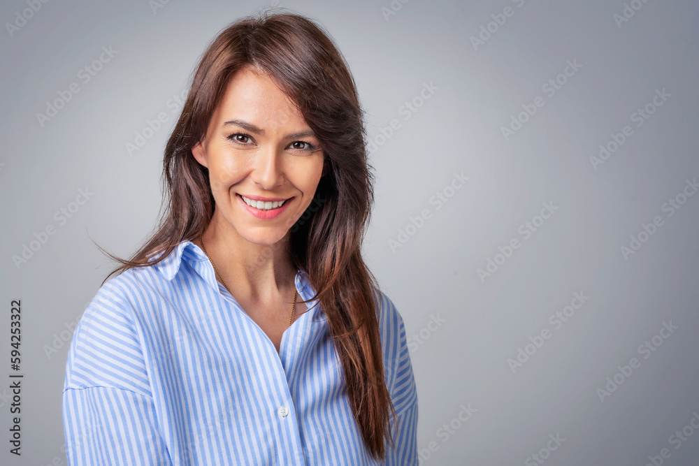 Studio portrait of attractive woman wearing shirt and laughing while sitting at isolated grey background. Studio portrait of attractive woman wearing shirt and laughing while sitting at isolated grey background.