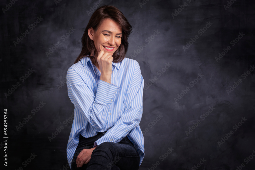 Studio portrait of attractive woman wearing shirt and laughing while standing at isolated dark background. Studio portrait of attractive woman wearing shirt and laughing while standing at isolated dark background.
