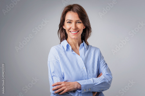 Studio portrait of attractive woman wearing shirt and laughing while sitting at isolated grey background.