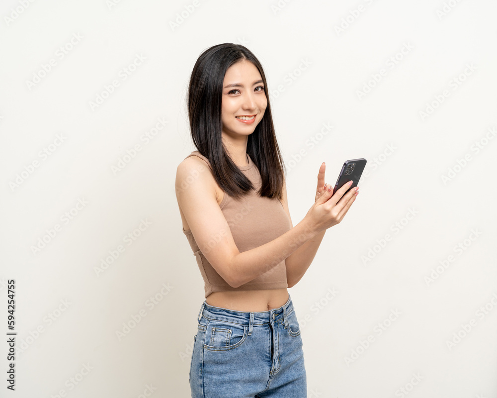 Pretty young asian woman using smartphone standing on isolated white background. Excited Beautiful young asian shopping online payment with mobile phone. Playing game on smartphone Pretty young asian woman using smartphone standing on isolated white background. Excited Beautiful young asian shopping online payment with mobile phone. Playing game on smartphone