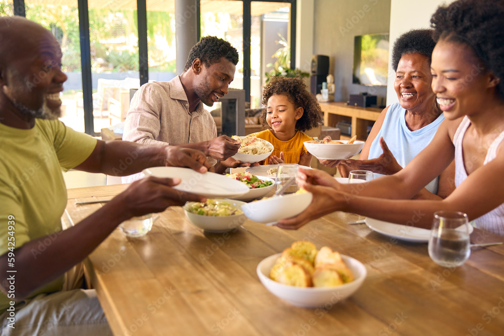 Multi-Generation Family Sitting Around Table Serving Food For Meal At Home Multi-Generation Family Sitting Around Table Serving Food For Meal At Home