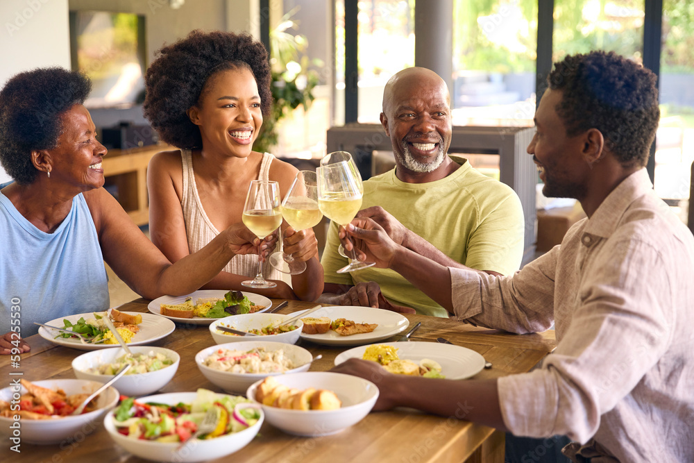 Family Shot With Senior Parents And Adult Offspring Around Table At Home Doing Cheers Before Meal