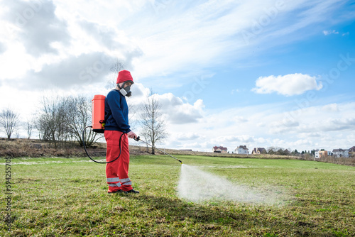 Farmer spraying pesticide on lawn field wearing protective clothing. Treatment of grass from weeds and dandelion. Pest control. Insecticide sprayer with a proper protection. Gardening care season