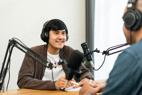 Young asian man host streaming podcast with condenser microphone work on tablet at small broadcast home studio. Content creator blogger recording voice over radio interview guest conversation