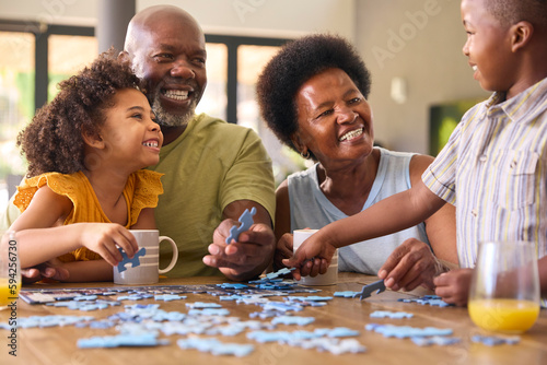 Family Shot With Grandparents And Grandchildren Doing Jigsaw Puzzle On Table At Home
