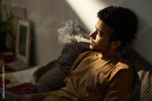 Young man in melancholy smoking and thinking about his problems alone sitting in the room