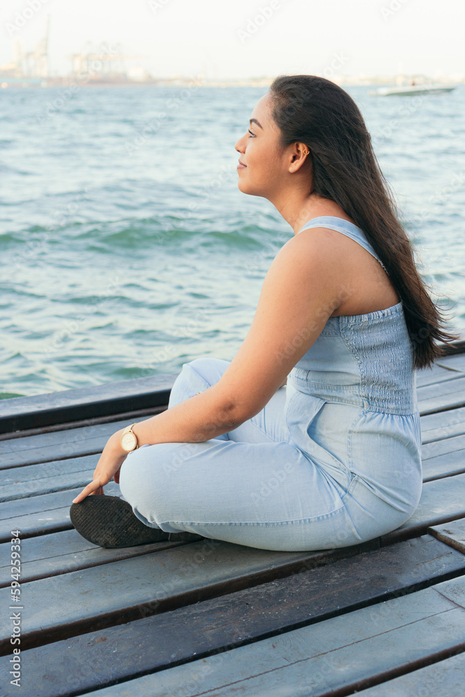 Young Woman pensive while sitting on a lake dock during a beautiful summer day.