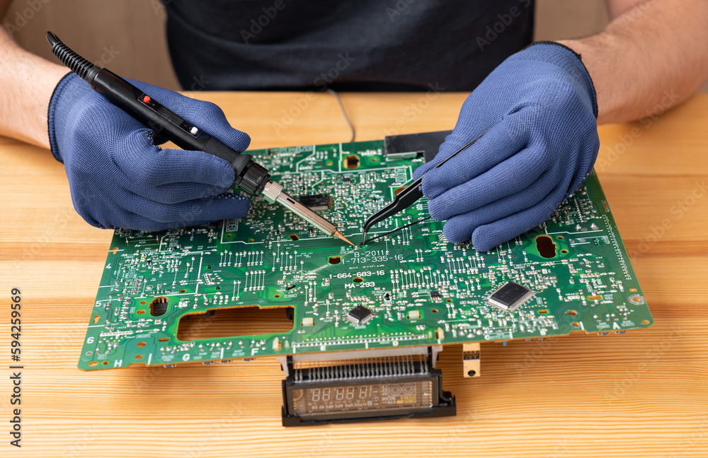 A man holds a soldering iron in his hand and solders a microcircuit