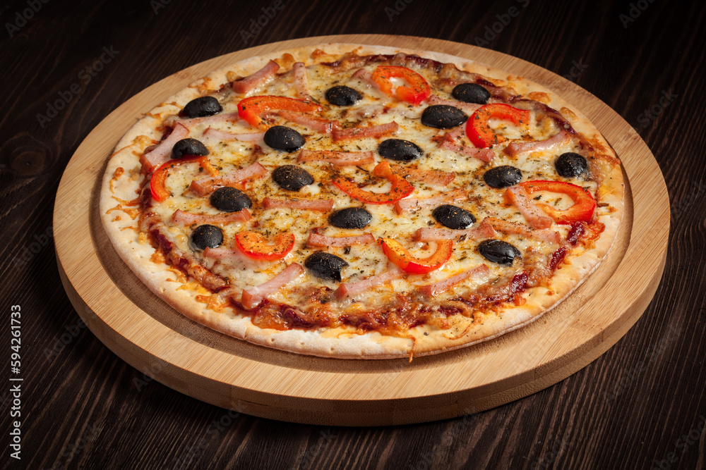 Ham pizza with capsicum and olives on wooden board on table