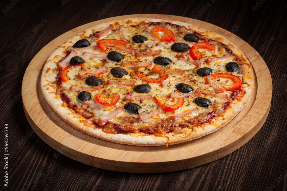 Ham pizza with capsicum and olives on wooden board on table Ham pizza with capsicum and olives on wooden board on table