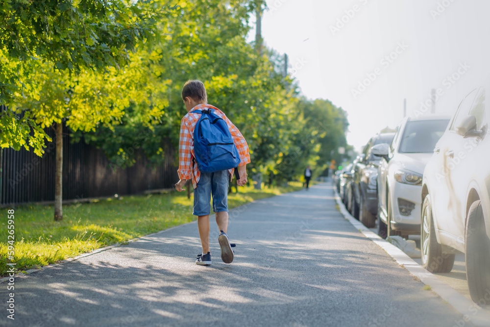 back view of caucasian boy walking from school wearing school bag. Begining of academic year back view of caucasian boy walking from school wearing school bag. Begining of academic year