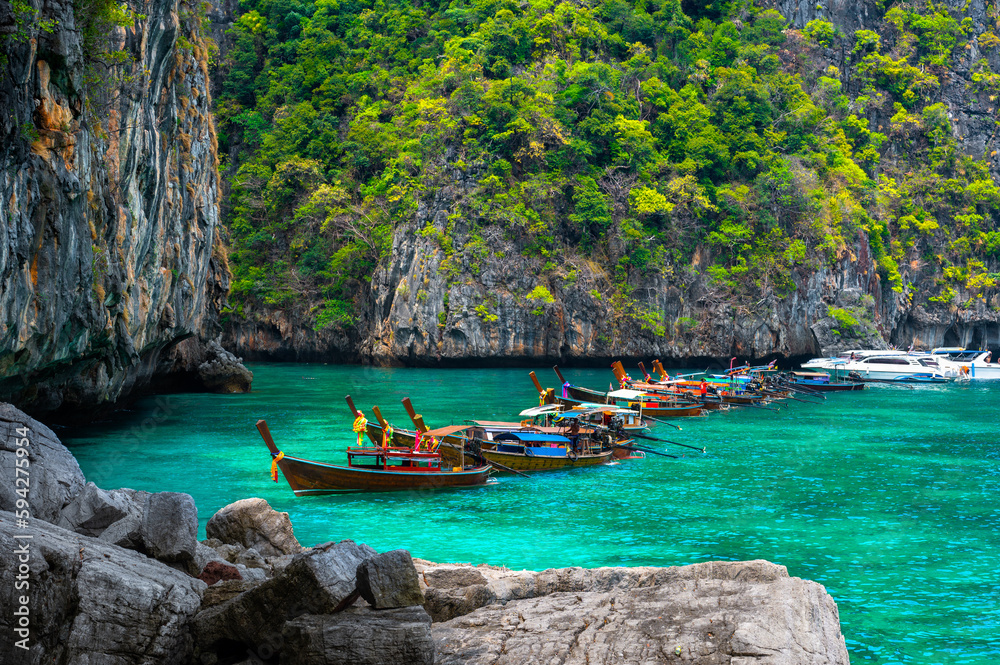 Many traditional longtail boats parking at Maya Bay, Ko Phi Phi Leh island, part of Krabi, Thailand. View round with steep limestone hills and emerald green water. Many traditional longtail boats parking at Maya Bay, Ko Phi Phi Leh island, part of Krabi, Thailand. View round with steep limestone hills and emerald green water.