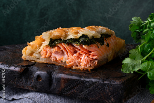 Pie with trout and spinach filling in puff pastry served on dark wooden board photo