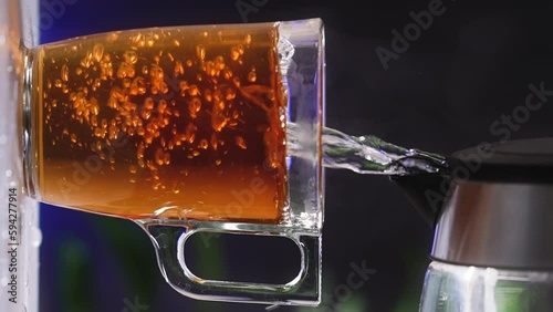 Glass cup of tea, black tea bag dissolves in hot water. Steam from boiling water. Transparent glass. Morning tea. Vertical video slow motion 4k