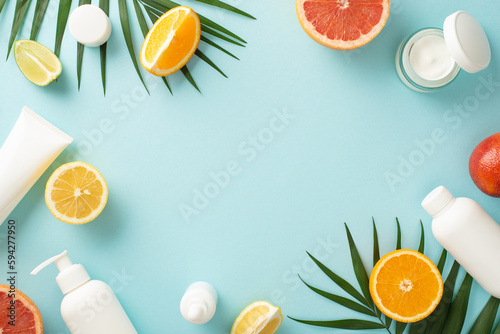 Citrus summer beauty concept. Top view flat lay of mock up cream bottles, jars, serum, pipette with orange, grapefruit, lemon, flower on blue background with empty space for text. Stylish and juicy