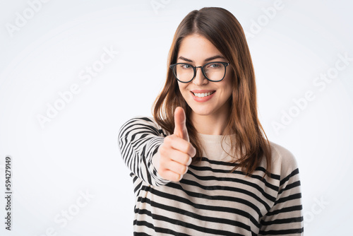 Cheerful smiling young woman giving thumbs up and standing at isolated white background