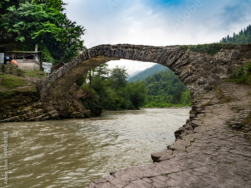 Ancient stone arched bridge across the river in Georgia. Popular tourist spot. Mountains in the background. No people