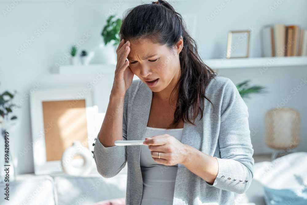Worried stressful woman looking at predictor finding out she is pregnant at home Worried stressful woman looking at predictor finding out she is pregnant at home