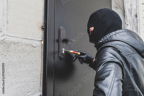A burglar opens the lock on the iron door of a country house. A criminal concept. Burglary. Burglar breaking into house