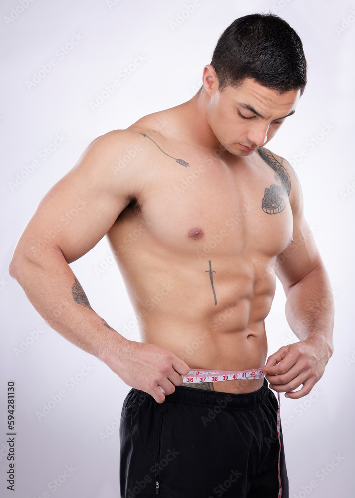 Ive lost so much weight. a young muscular man measuring his waist against a grey studio background.