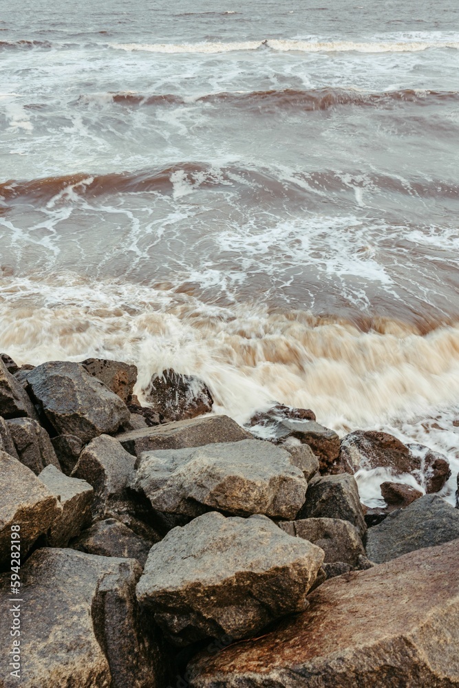 Fototapeta premium Vertical shot of waves crashing on the massive rocks on the beach, perfect for wallpapers