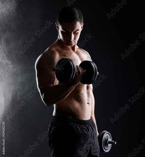 Lift and live life with no regrets. an athletic man lifting dumbbells against a dark background.