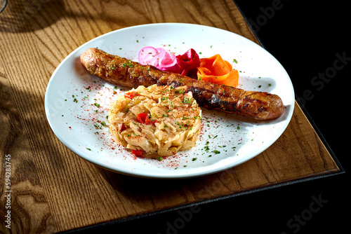 Bavarian meat sausage with a garnish of stewed sauerkraut, onions in a plate on a wooden background