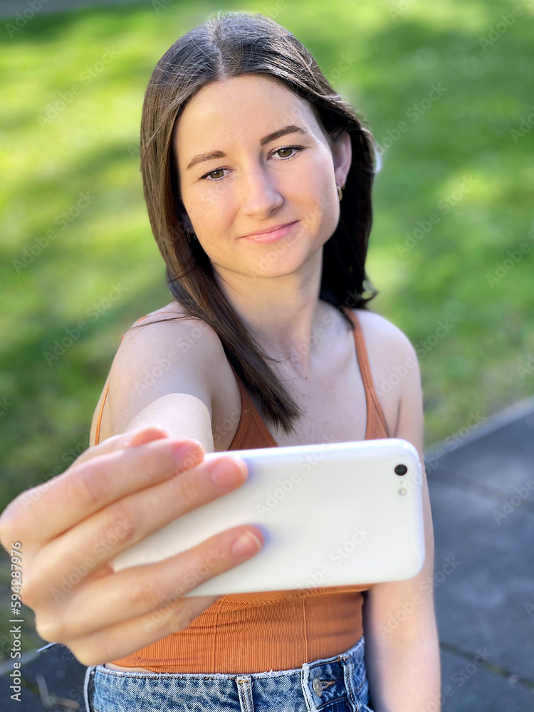 Young woman outdoors in park takes a selfie with her smartphone camera
Young woman outdoors in park takes a selfie with her smartphone camera