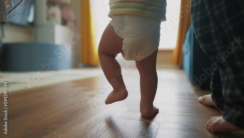 baby takes the first steps to learn. happy family kid dream concept. mom teaches baby newborn to walk and take first steps. mom light holding baby hands teaches to walk silhouette from window