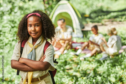 Waist up portrait of cute black girl scout looking at camera while camping with school group, copy space