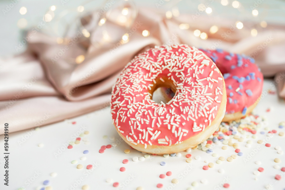 Two fresh sweet glazed donuts on the table, the background is decorated with draped fabric and bokeh Two fresh sweet glazed donuts on the table, the background is decorated with draped fabric and bokeh