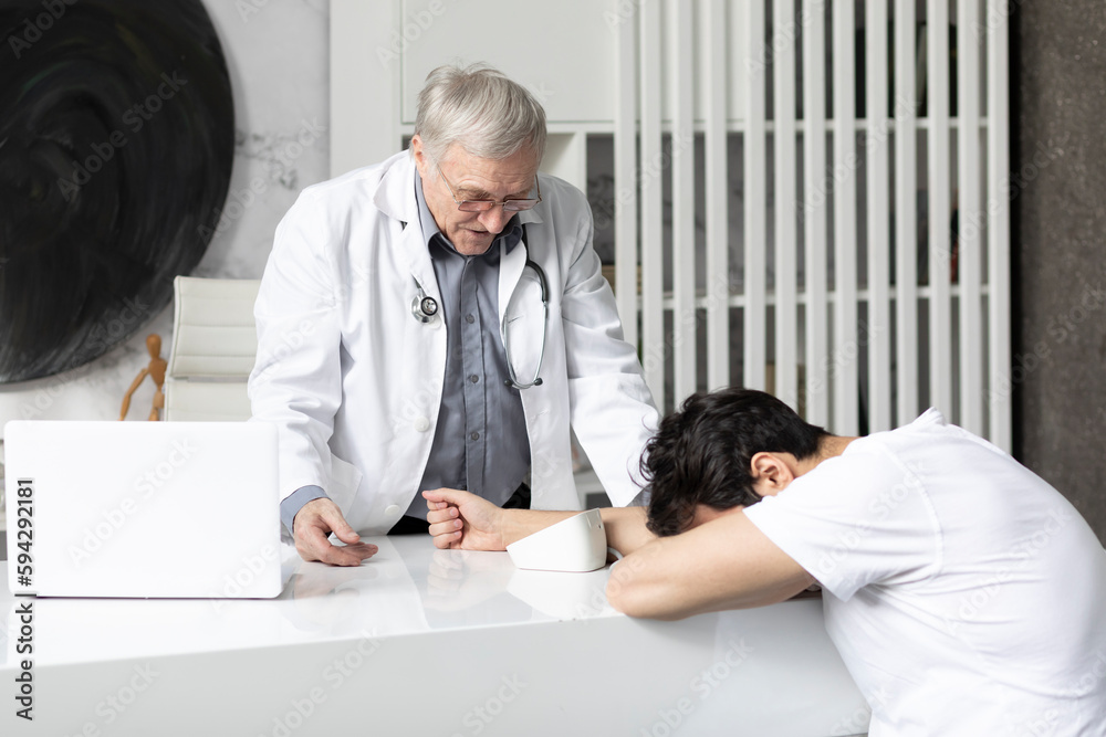 Senior doctor is measuring with tonometer blood pressure of his young patient in modern medical office Senior doctor is measuring with tonometer blood pressure of his young patient in modern medical office