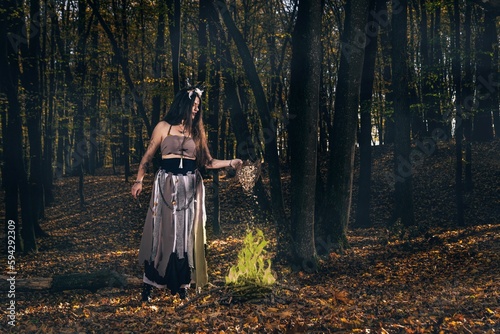 Young female with long hair and face paint in a witch costume casting a spell in a forest
