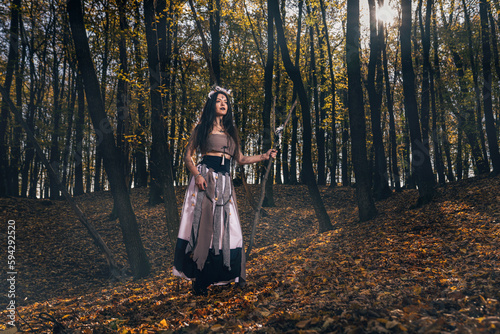 Young female with long hair and face paint in a witch costume casting a spell in a forest © Ionut Dragoi/Wirestock Creators