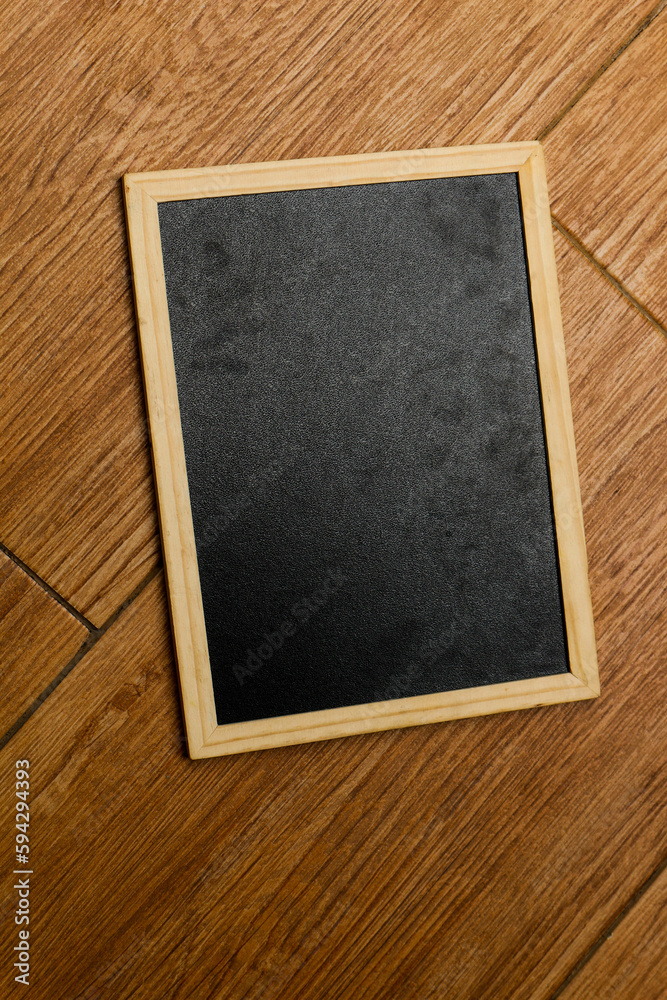 A small black chalkboard with a wooden frame rests on a wooden textured floor. A small black chalkboard with a wooden frame rests on a wooden textured floor.