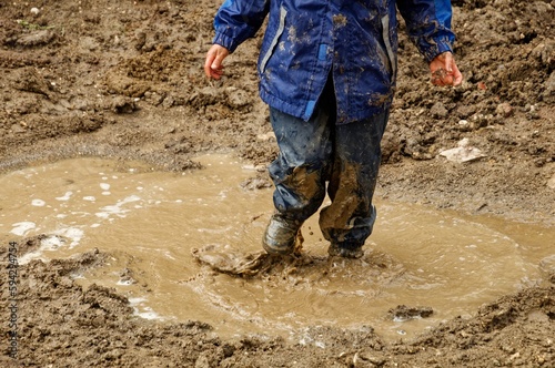 Boy joyfully standing in mud on rainy day, enjoying nature, Germany