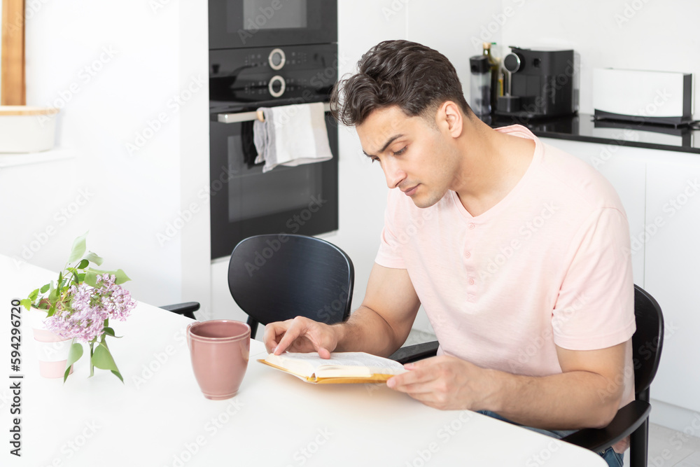 Young handsome man reading book and drinking tea in the kitchen Young handsome man reading book and drinking tea in the kitchen