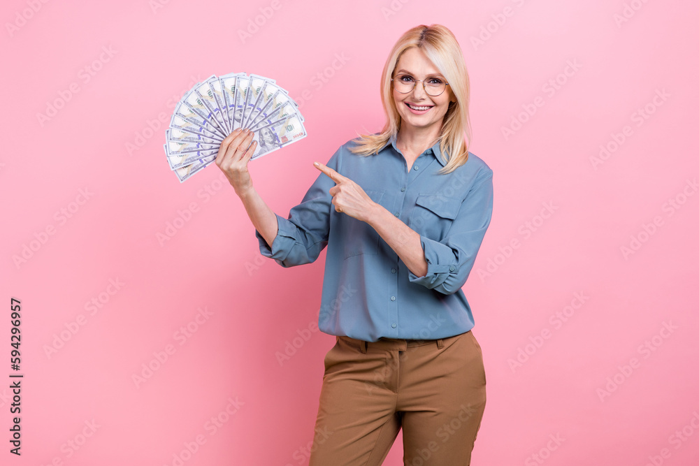 Photo of promoter elderly business lady wear blue shirt formal clothes direct finger much money investment idea isolated on pink color background Photo of promoter elderly business lady wear blue shirt formal clothes direct finger much money investment idea isolated on pink color background