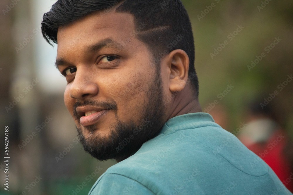 Indian male stands facing the camera while smiling and gazing off into the distance