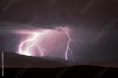 Dramatic image of a stormy sky above a mountain range, illuminated by a brilliant lightning bolt