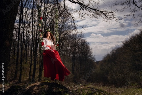 Young beautiful woman in a red skirt is posing on a swing in a park