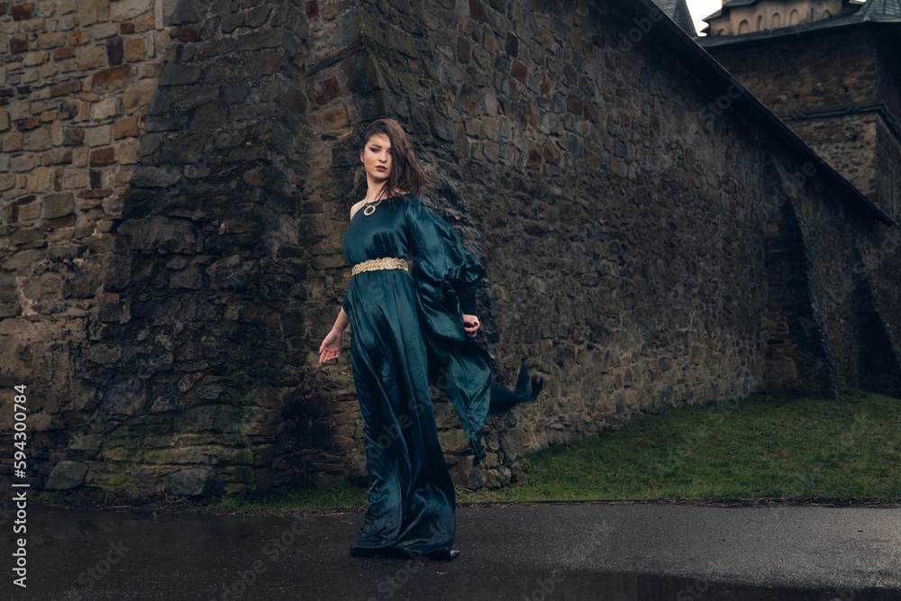 Young beautiful female in a medieval green dress posing near ancient ruins
