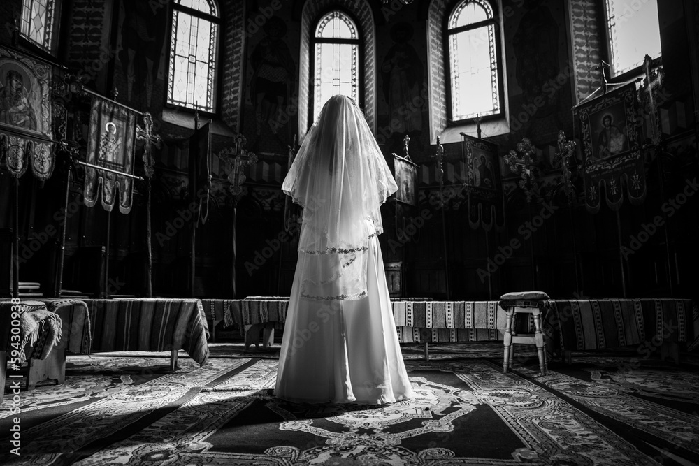 Grayscale shot of a young woman in a wedding dress standing in front of the altar.
